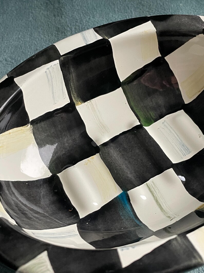 May include: A black and white chequered ceramic serving dish. The dish has a glossy finish and a slightly raised rim. The pattern is a classic checkerboard design, with alternating black and white squares. The dish is oval-shaped.