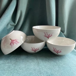 May include: Four white ceramic bowls with pink magnolia flower designs. The bowls are stacked on top of each other.