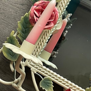 May include: White metal wall mirror with a floral design. The mirror has a rope-like border and two pink candlesticks. The candlesticks are decorated with pink roses.