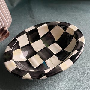 May include: Oval ceramic dish featuring a black and white chequered design. The dish has a shallow, curved interior and a glossy finish. The rim is painted cream. This decorative dish is suitable for holding small items, such as soap.