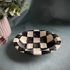 May include: An oval ceramic bowl featuring a black and white chequered design. The bowl has a glossy finish and a raised rim. The interior is plain white. This bowl is likely for serving or display purposes. The bowl's dimensions are approximately 20 cm in length.