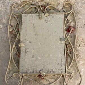 May include: White metal picture frame with a floral design. The frame has a white background with red accents. The frame is designed to hang on a wall.