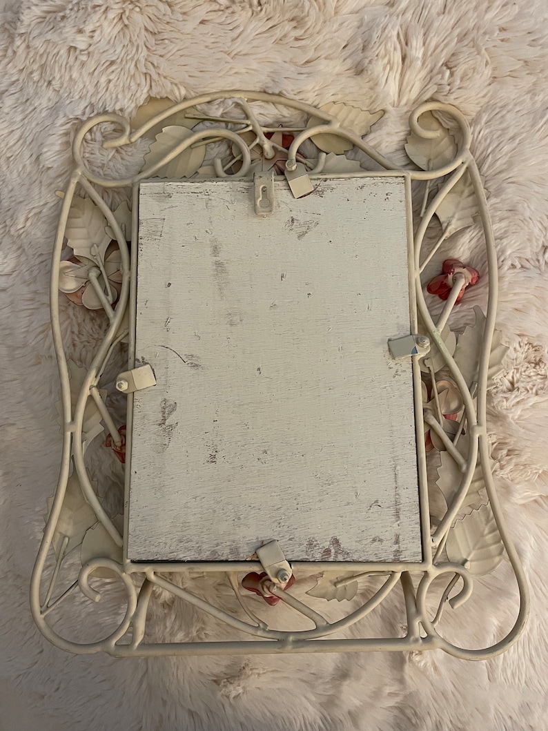 May include: White metal picture frame with a floral design. The frame has a white background with red accents. The frame is designed to hang on a wall.