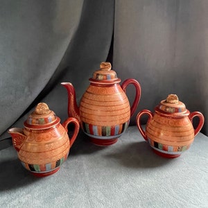 May include: A red and gold tea set with a teapot, creamer, and sugar bowl. The set is decorated with a geometric pattern and gold accents.