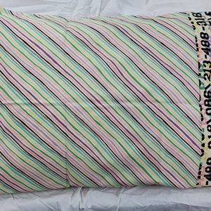 May include: A white pillowcase with diagonal stripes in pink, green, blue, and purple. The edge of the pillowcase has a black border with a repeating pattern of numbers.