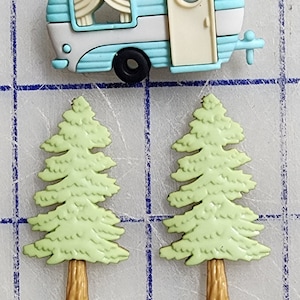 May include: Two green plastic pine trees with brown trunks and a blue and white plastic camper with a white door and a window. The camper has a black tire and a white hitch.