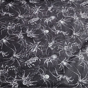 May include: Black fabric with a white spider web and spider pattern. The fabric is measured with a ruler in inches.