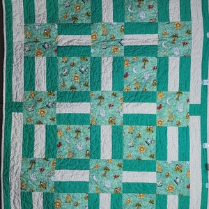 May include: A green and white baby quilt with a patchwork design featuring various animal prints. The quilt is made of cotton fabric and has a quilted texture.