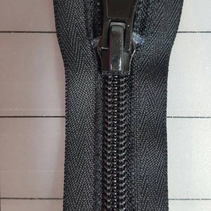 May include: A black zipper with a black metal slider and pull tab. The zipper is closed and the teeth are visible.