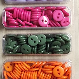 May include: A package of 300 assorted plastic buttons in six colors: purple, yellow, orange, green, pink, and blue. The buttons are 3/8 inch (9mm) in diameter and have two holes. The package is labeled "Sew-ology Buttons".