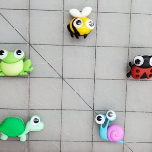 May include: Five colorful plastic animal figurines with googly eyes. A green frog, a yellow and black bee, a red ladybug, a green turtle, and a blue and pink snail.