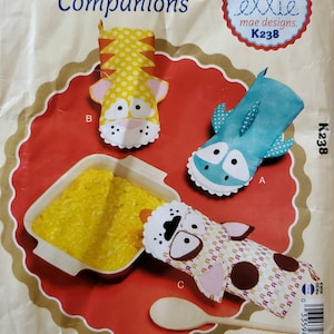 May include: A sewing pattern for quilted pot holders featuring a tiger, a shark, and a dog. The pattern is called "Quilted Cooking Companions" and is by ellie mae designs. The pattern number is K238.