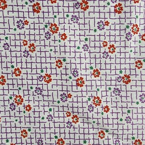 May include: A white fabric featuring a repeating pattern of small red and purple flowers with tiny green dots. The background is overlaid with a purple grid of thin, intersecting lines that create a structured, woven-like appearance across the surface.