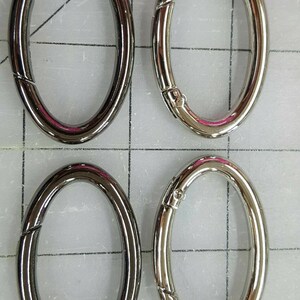May include: Four oval-shaped metal clasps. Two are a dark gunmetal color, and two are silver. Each clasp has a hinged opening mechanism. The clasps are arranged in a 2x2 grid.