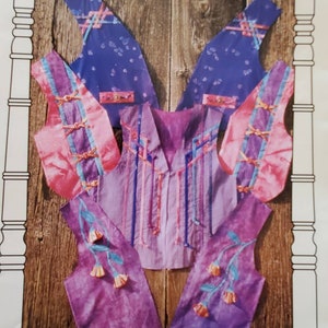 May include: A sewing pattern for a vest with a purple, pink, and blue floral design. The pattern is called "Knot Your Average Vest" and is from Homestead Specialties. The pattern is for sizes S, M, L, and XL.
