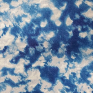 May include: A white fabric with a blue tie-dye pattern. The fabric has a subtle texture and a light blue color.