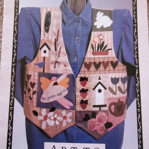 May include: A patchwork quilt vest with a variety of designs, including hearts, flowers, birds, and a teapot. The vest is displayed on a mannequin wearing a blue shirt. The text "You garden angel" is embroidered on the vest. The text "ART-TO HEART" and "NANCY HALVORSEN (801)544-5511" is printed on the bottom of the image.