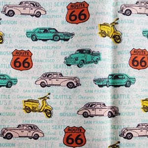 May include: A light blue background with a repeating pattern of vintage cars, motorcycles, and Route 66 signs. The cars are in shades of pink, green, and blue. The motorcycles are yellow. The signs are orange with black lettering.
