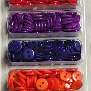 May include: A package of 300 assorted plastic buttons in six colors: red, purple, blue, orange, green, and yellow. The buttons are 3/8 inch (9mm) in diameter and have two holes. The package is labeled "Sew-ology Buttons".