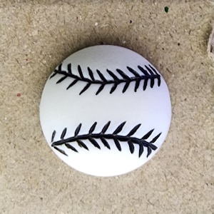 May include: White baseball with black stitching. The stitching is in the shape of a baseball seam.