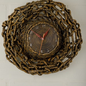 Puede incluir: Un reloj tejido marrón con una cara circular y marcas de números romanos negros. Las manecillas del reloj son rojas y naranjas.