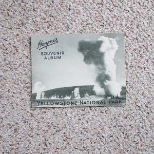 Può includere: Una foto in bianco e nero di un geyser in eruzione nel Parco Nazionale di Yellowstone. La foto è su un album di souvenir vintage Harpers.