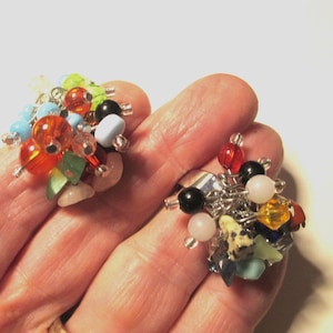 May include: A pair of colourful cluster earrings. Each earring features a mix of beads in various colours, including orange, blue, green, black, and white. The beads are clustered together with silver-tone metal findings.