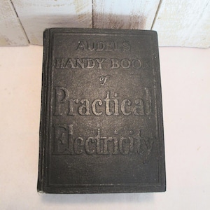 Könnte beinhalten: Ein schwarzes Hardcover-Buch mit dem Titel "AUDEL'S HANDY BOOK of Practical Electricity". Der Titel ist auf dem Einband geprägt. Das Buch ist rechteckig und scheint vintage zu sein.