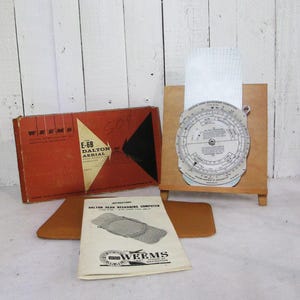 May include: A Weems E-6B Dalton Aerial Dead Reckoning Computer set including a red and black cardboard box, a circular metal flight computer mounted on a wooden stand, and an instructional booklet titled Dalton Dead Reckoning Computer.