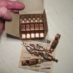 May include: A box of vintage Meller battery and test clips and connectors. The box is open and the clips are visible. The clips are made of copper and have a green insulator. The box is labeled "Meller Battery and Test Clips and Connectors".