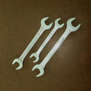 Puede incluir: Tres llaves inglesas Craftsman vintage de diferentes tamaños, dispuestas en diagonal sobre una superficie marrón. Las llaves son de un color verde claro descolorido, con el nombre de la marca visible en cada una. Herramientas para trabajos mecánicos o de reparación.