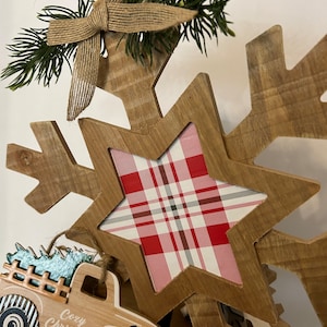 May include: Wooden Christmas decoration featuring a snowflake with a red and white plaid star in the center. A small wooden truck with a Christmas tree in the back says "Cozy Christmas".