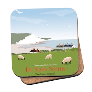 May include: A coaster featuring a scenic illustration of the Seven Sisters cliffs in East Sussex, England. The image depicts white cliffs, a blue sea, green fields, and sheep. The text "Forming part of the South Downs • THE SEVEN SISTERS • East Sussex, England" is printed on the coaster.