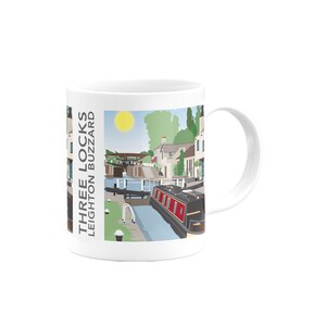 May include: White ceramic mug with a colorful illustration of a canal lock system and a narrowboat. The text "THREE LOCKS LEIGHTON BUZZARD" is printed on the side of the mug.
