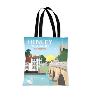 Puede incluir: Una bolsa de tela azul y blanca con un gráfico de Henley-on-Thames, Oxfordshire. El gráfico presenta un puente, edificios y cisnes. El texto "Henley on Thames Oxfordshire" está impreso en la bolsa.