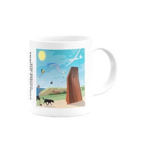 Puede incluir: Taza de cerámica blanca con una ilustración colorida de una persona paseando a un perro, un planeador en el cielo y un edificio alto y marrón. El texto "LUNNABLE DOWNS CHILTURN HILLS" está en el lateral de la taza.
