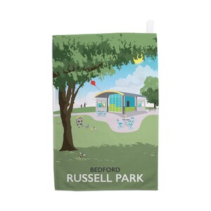 以下が含まれることがあります： 緑色のキッチンタオルに、公園の風景が描かれたイラストがプリントされています。イラストには、緑色の屋根と青い窓のある建物、緑の葉のついた木、空に赤い凧、下の方に飛んでいる蜂が描かれています。タオルの下部には黒い文字で「BEDFORD RUSSELL PARK」と印刷されています。