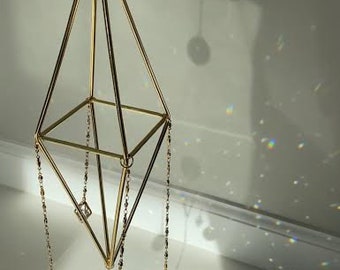 May include: A gold geometric hanging mobile with three crystal prisms. The mobile is suspended from a chain and has a diamond shape.