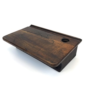 May include: A vintage wooden school desk with a dark brown finish. The desk features a sloped writing surface, a small hole for a pen or pencil, and a storage compartment. The desk is made of solid wood and has a classic, antique look.