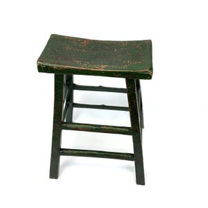 May include: A small wooden stool with a rectangular, slightly curved seat and four straight legs connected by horizontal stretchers. The stool features a dark green painted finish with visible signs of wear and distressed edges throughout.