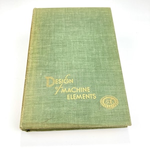 May include: A vintage book titled "Design of Machine Elements" with a green cover and gold lettering. The book has a textured appearance and a gold gear emblem. The book is closed and slightly worn.
