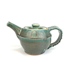 May include: A teal green ceramic teapot with a lid and a textured handle. The teapot has a rustic, handmade look.