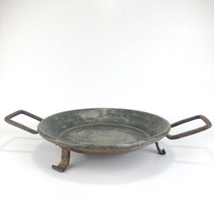 May include: A gray metal serving tray with two handles and three legs. The tray is made of metal and has a rustic look.