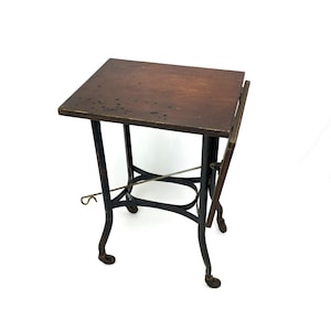 May include: A rectangular wooden side table with a dark brown finish and a drop-leaf side. The table features a black metal base with four curved legs, each ending in a small caster wheel, and a thin metal support rod extending horizontally.