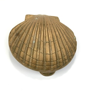 May include: A gold-colored metal seashell trinket box with a detailed, textured surface.