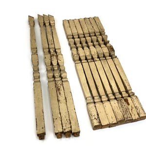 May include: A set of antique wooden spindles with a distressed white paint finish. The spindles are approximately 18 inches long and have a decorative turned design.
