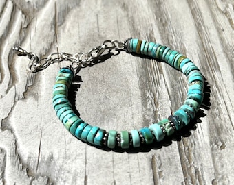 May include: A turquoise and silver bracelet with a chain clasp. The bracelet is made of small, round turquoise beads.