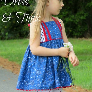 May include: A young girl wearing a blue and red sleeveless dress with a white and blue firework print. The dress has red straps and a red trim. The girl is holding a bouquet of white flowers. The text "Firecracker Dress & Tunic" is written in white cursive at the top of the image. The text "GYCT Designs" is written in black cursive at the bottom of the image.
