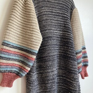 May include: A gray and beige striped sweater with long sleeves. The sleeves have a multi-colored stripe pattern in shades of blue, pink, and beige.