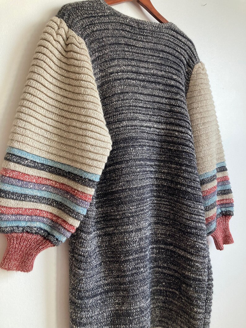 May include: A gray and beige striped sweater with long sleeves. The sleeves have a multi-colored stripe pattern in shades of blue, pink, and beige.